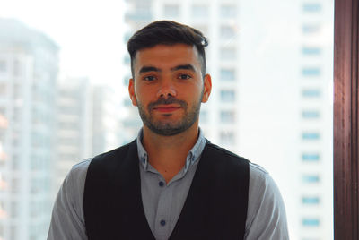 Portrait of young man standing against window