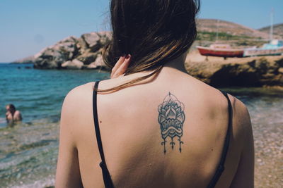 Rear view of woman showing tattoo while standing at beach