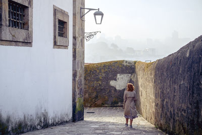 Rear view of woman walking on wall against building