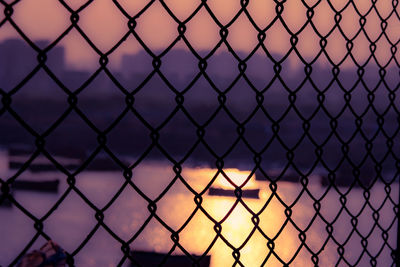 Close-up of chainlink fence against sky during sunset