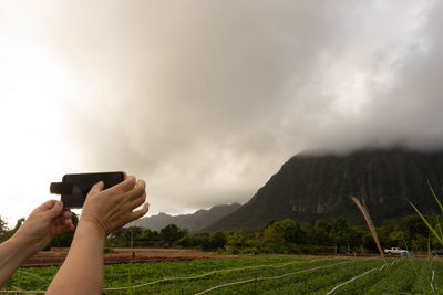 Man photographing with mobile phone against sky