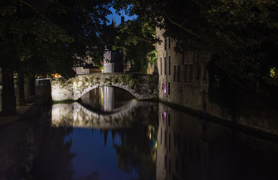 Arch bridge over river amidst buildings at night