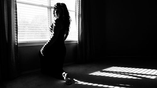 Portrait of woman sitting by window at home on sunny day