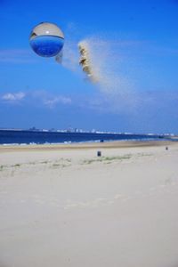 Hot air balloon flying over beach against blue sky