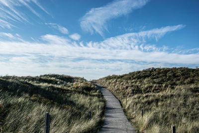 Boardwalk leading towards landscape against sky