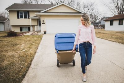 Full length of woman with garbage bin walking on footpath