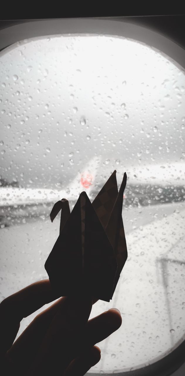 CLOSE-UP OF HAND HOLDING GLASS WINDOW IN RAIN
