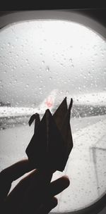 Close-up of hand holding glass window in rainy season