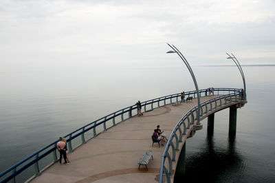 People on pier over sea against sky