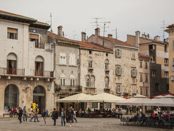 People walking by buildings in city against clear sky