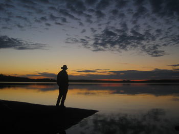 Silhouette man standing on lake against sky during sunset