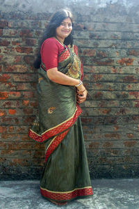 Portrait of a smiling young woman standing against brick wall