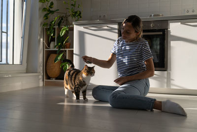 Young woman owner enjoy taking care of beloved cat and combing it sits on floor at home. pet lovers