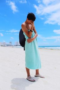 Teenage boy wearing towel while standing at beach against blue sky