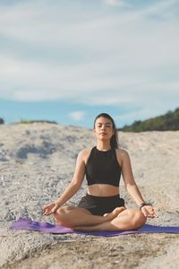 Young woman sitting on sand at beach against sky