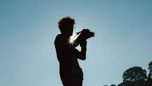 Low angle view of man photographing against clear sky