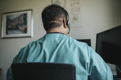 Rear view of doctor wearing headset using computer during online consultation