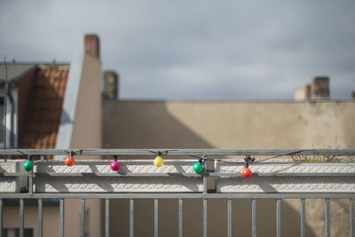 Multi colored light bulbs on railing by building against sky