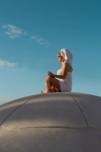 Low angle view of woman sitting on road against sky
