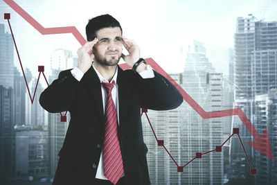 Tensed businessman standing against graph and buildings in city