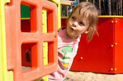 Surprised happy child peeking out of a small house in the playground. play hide-and-seek