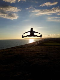 Silhouette man jumping at beach against sky