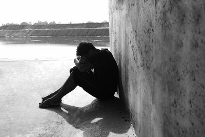 Side view of man sitting on concrete wall