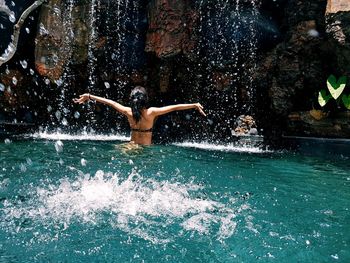 Rear view of woman below waterfall in forest