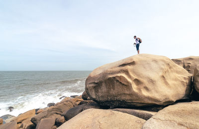 Man on rock by sea against sky