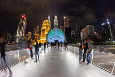 People on illuminated modern buildings in city at night