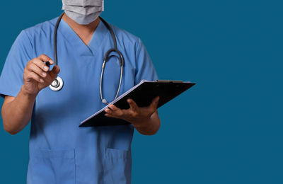 Midsection of doctor holding clipboard against blue background