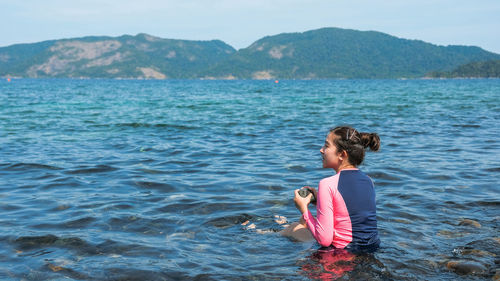 Rear view of young woman looking away while sitting in sea