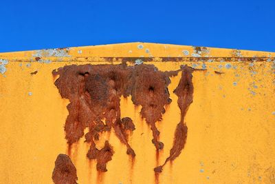 Shadow of rusty metal on wall against clear blue sky