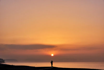 Silhouette people standing by sea against sky during sunset