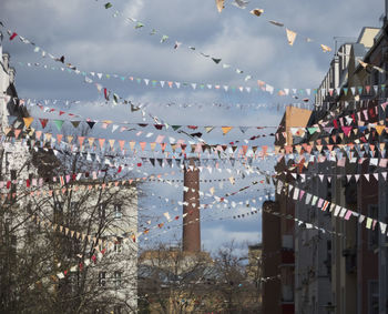 Low angle view of flags hanging amidst trees and buildings against sky