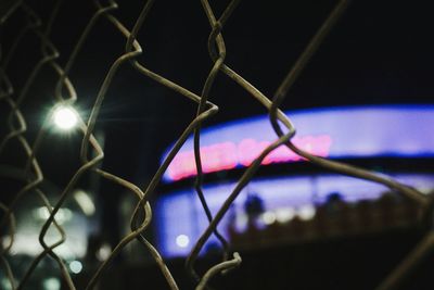 Close-up of chainlink fence against sky at night