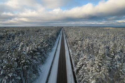Aerial view of asphalt highway leading through frosty winter forests and groves covered with snow