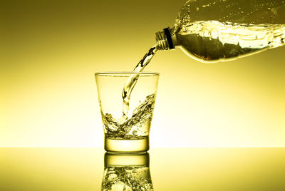 Bottle pouring drink in glass on table against wall