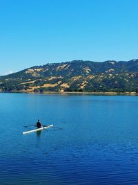 Man kayaking in lake against mountains and clear sky