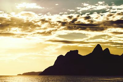 Silhouette rocks by sea against sky during sunset