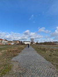 People on road amidst field against sky