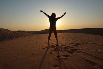 Man standing on sand at beach against sky during sunset