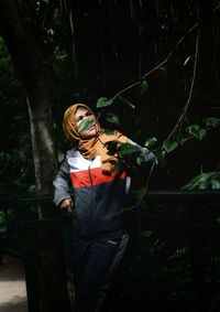 Woman in headscarf standing by tree in forest