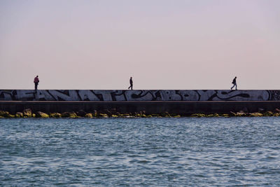 People walking on pier against clear sky