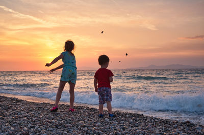 Summer memories. children throwing pebbles to sea during sunset.