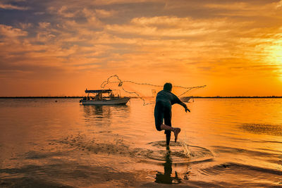 Silhouette man fishing in sea against sky during sunset