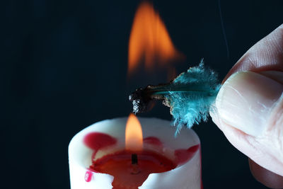 Close-up of hand holding lit candle against black background