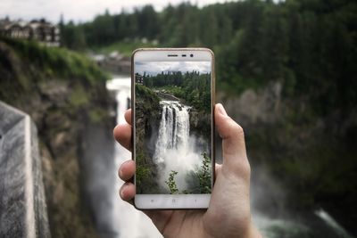 Cropped hand photographing waterfall with mobile phone