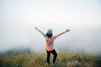 Rear view of woman with arms outstretched standing on mountain during foggy weather