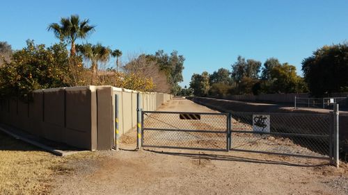 Closed gate on empty road against clear blue sky